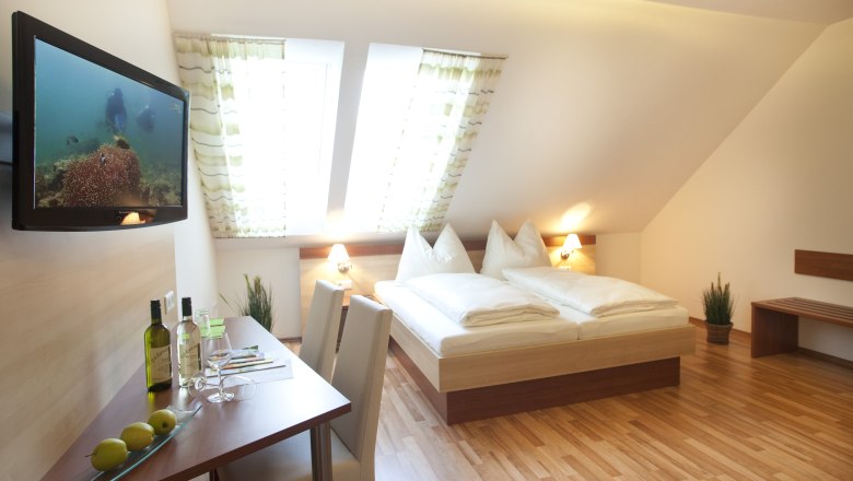 Ein gemütliches Gästezimmer mit Doppelbett, Flachbildfernseher, Tisch mit Stühlen und Dachfenstern.