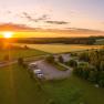 Luftaufnahme eines Wohnmobilstellplatzes bei Sonnenuntergang, umgeben von Feldern und W&auml;ldern.
