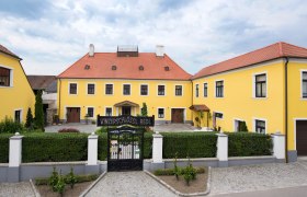 Gelbes Gebäude mit rotem Dach und Tor mit der Aufschrift 'Winzerschlössl Redl'.