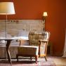 Gemütliches Zimmer mit Sessel, Tisch und Stehlampe vor einem Bett mit rustikaler Holzverkleidung.