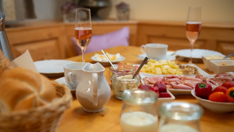 Frühstückstisch mit Brötchen, Aufschnitt, Käse, Sektgläsern und Joghurt.