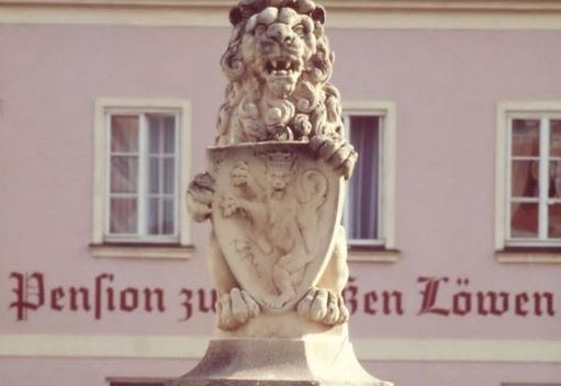 Steinlöwe mit Wappen vor einem Gebäude mit der Aufschrift 'Pension zum Weißen Löwen'.
