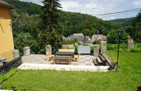 Terrasse mit Holzm&ouml;beln und Blick auf ein Dorf und bewaldete H&uuml;gel.