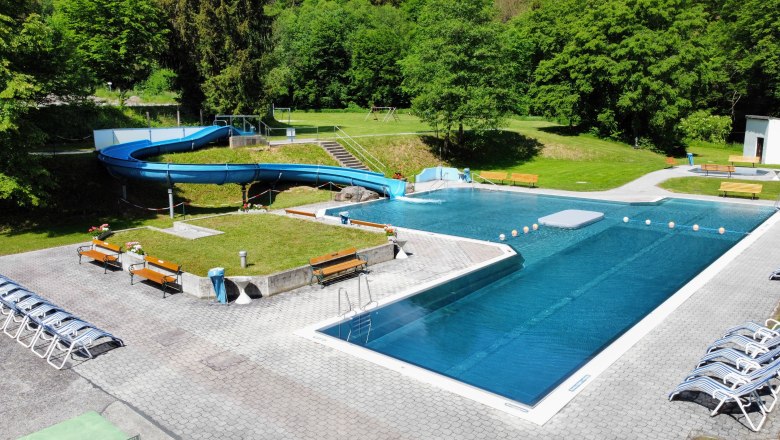 Ein Freibad mit Rutsche und Liegest&uuml;hlen, umgeben von B&auml;umen.