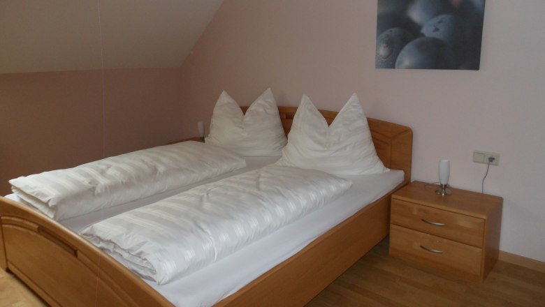 Ein schlichtes G&auml;stezimmer mit einem Doppelbett, wei&szlig;en Bettdecken und einem Nachttisch mit Lampe.