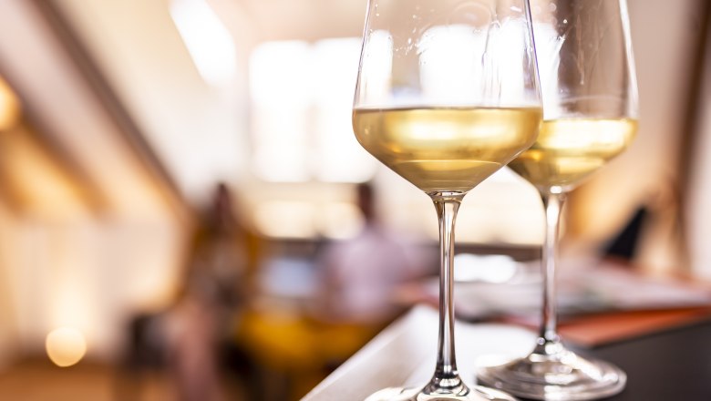 Zwei Gläser Weißwein auf einem Tisch, unscharfer Hintergrund.