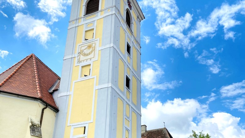 Schiefer Turm in Waitzendorf mit gelber Fassade und Uhr, umgeben von blauen Himmel und Wolken.
