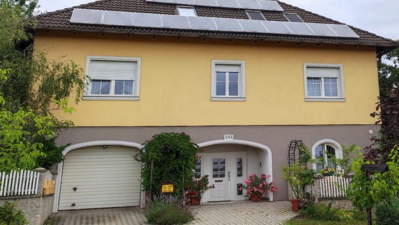 Privatzimmer Kahrer, © Kahrer Gelbes Haus mit Solarpanels auf dem Dach, Garage und Eingang mit Blumen.