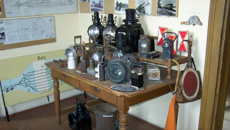 Ein Tisch mit alten Eisenbahnlampen und Signalen in einem Raum mit historischen Plänen an der Wand.