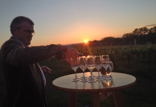 Ein Mann schenkt Wein in Gläser auf einem Tisch bei Sonnenuntergang in einem Weinberg ein.
