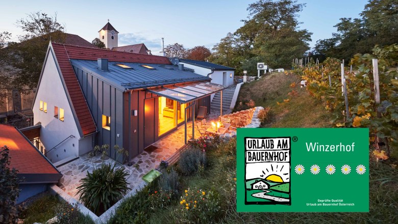 Ein modernes Kellerst&ouml;ckl im Weinviertel bei D&auml;mmerung, umgeben von Weinreben und einem Garten. Ein Schild zeigt 'Urlaub am Bauernhof'.