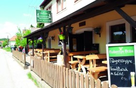 Außenansicht eines Heurigen-Restaurants mit Holztischen und einer Tafel mit Tagesangeboten.