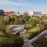 Ein gepflegter Garten mit Bäumen, Blumen, einem Tisch mit Stühlen und zwei Liegestühlen. Im Hintergrund sind moderne Häuser zu sehen.