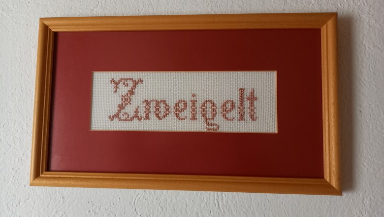 Stickbild mit dem Wort 'Zweigelt' in einem Holzrahmen.