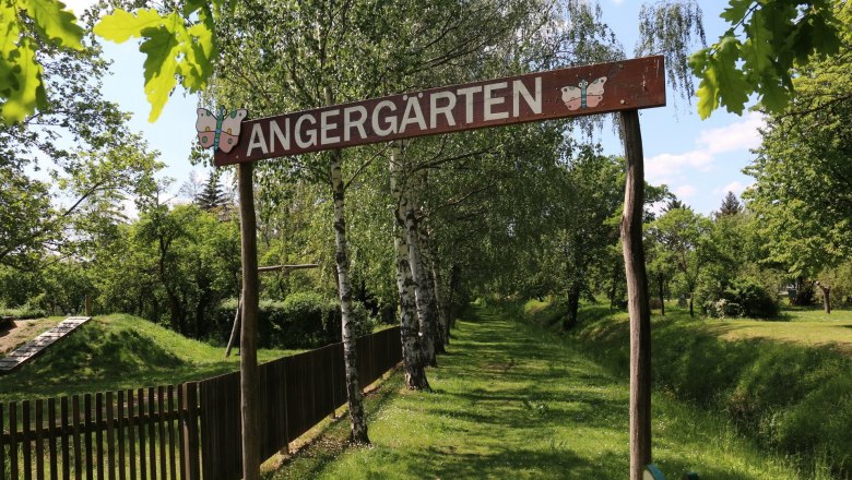 Eingang zu den Angergärten mit Holzschild und Bäumen im Hintergrund.
