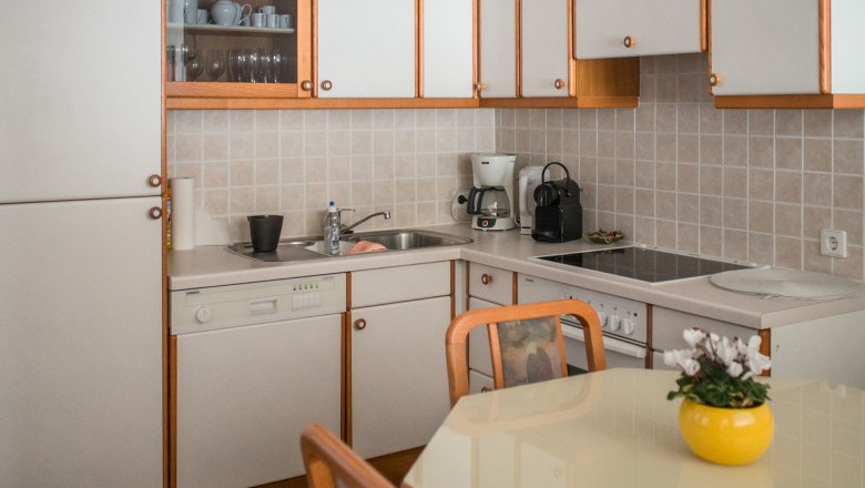 Moderne K&uuml;che mit wei&szlig;en Schr&auml;nken, Geschirrsp&uuml;ler, Kaffeemaschine und Herd. Gelber Blumentopf auf dem Tisch.