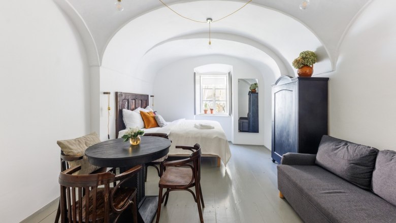 Gästezimmer, © Fam. Sebök Ein stilvoll eingerichtetes Gästezimmer mit gewölbter Decke, Bett, Sofa, Tisch und Stühlen. Ein Fenster lässt Tageslicht herein.