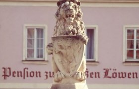 Steinlöwe mit Wappen vor einem Gebäude mit der Aufschrift 'Pension zum Weißen Löwen'.