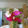 Ein Blumenstrau&szlig; mit rosa und wei&szlig;en Bl&uuml;ten steht in einer Vase auf einem Tisch in einer K&uuml;che.