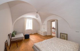 Gewölbezimmer mit Holzboden, Bett, Sofa und Fenster.