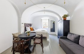 Ein stilvoll eingerichtetes Gästezimmer mit gewölbter Decke, Bett, Sofa, Tisch und Stühlen. Ein Fenster lässt Tageslicht herein.