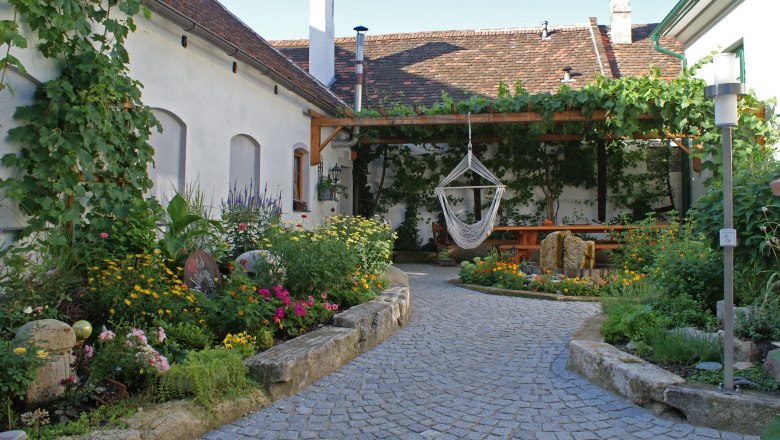 Ein idyllischer Innenhof mit Blumenbeeten, einer Hängematte und einem überdachten Sitzbereich.