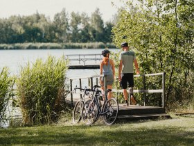 Zwei Personen gehen Richtung Bergwerksee entlang eines Stegs, ihre R&auml;der haben sie vorher abgestellt
