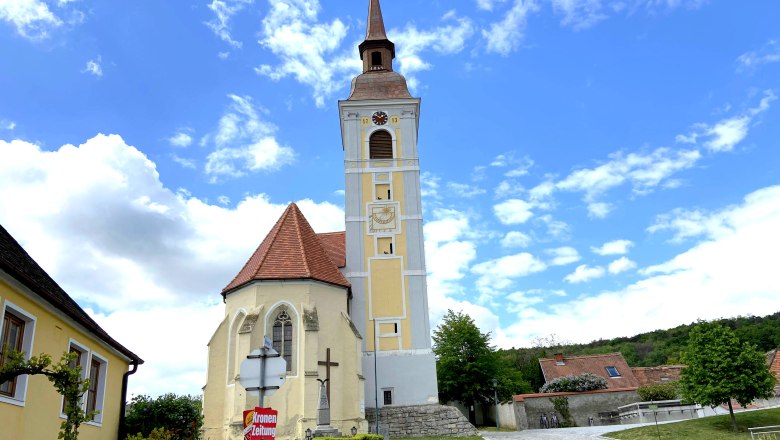 Kirche mit schiefem Turm in Waitzendorf, umgeben von blauen Himmel und Wolken.