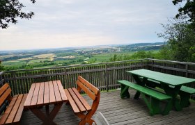Aussichtsplattform mit Holzb&auml;nken und Tischen, Blick auf weite Landschaft und Felder.