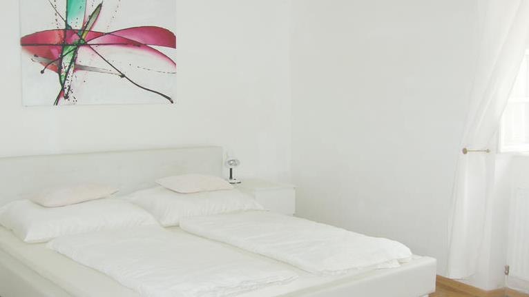 Helles Schlafzimmer mit Doppelbett und abstraktem Kunstwerk an der Wand.