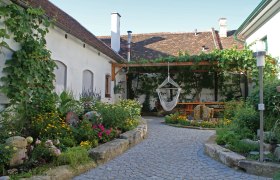 Ein idyllischer Innenhof mit Blumenbeeten, einer Hängematte und einem überdachten Sitzbereich.