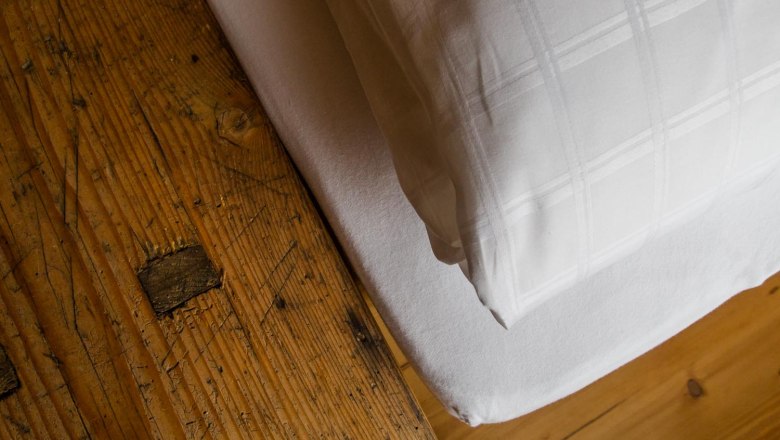Nahaufnahme eines rustikalen Holztisches neben einem Bett mit weißer Bettwäsche.