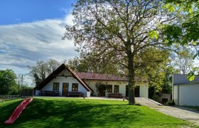 Ein Weingut mit Terrasse, Bäumen und einer Rutsche im Vordergrund.