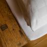 Nahaufnahme eines rustikalen Holztisches neben einem Bett mit weißer Bettwäsche.