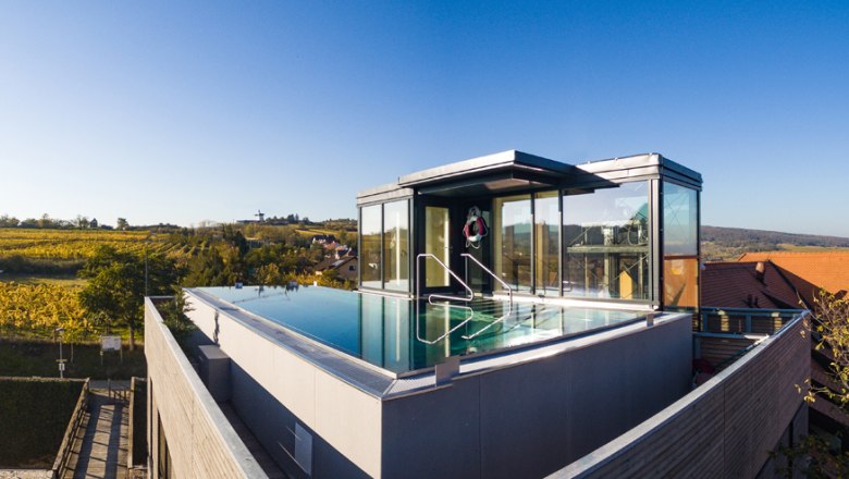 Ein moderner Dachpool mit Glasw&auml;nden und Blick auf eine herbstliche Landschaft mit Weinbergen.