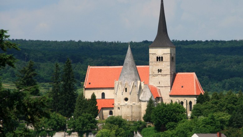 St. Michaelskirche in Pulkau mit rotem Dach und spitzem Turm, umgeben von B&auml;umen.