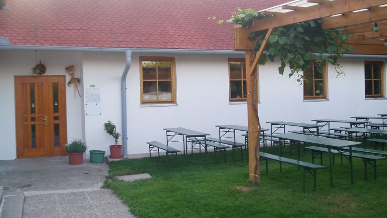 Ein Garten mit Biertischen, einem Holzpergola und einem Gebäude mit roten Dachziegeln.