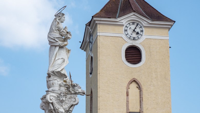Kirchturm mit Uhr und Mariens&auml;ule in Schrattenthal vor blauem Himmel.