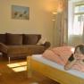 Ein Kind liegt l&auml;chelnd auf einem Bett in einem gem&uuml;tlichen Zimmer mit Sofa und Bild an der Wand.