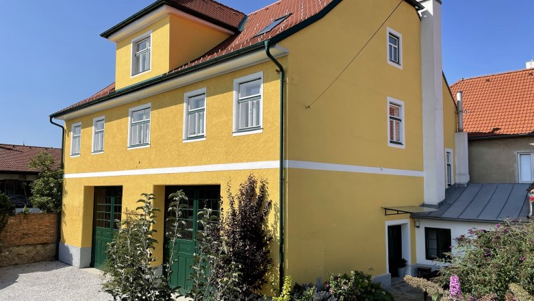 Gelbes zweistöckiges Haus mit rotem Dach und Garten.