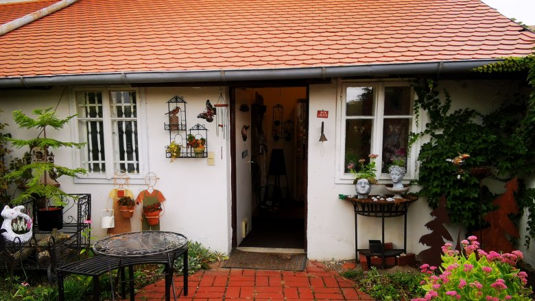 Eingang eines Hauses mit roten Dachziegeln, dekoriert mit Pflanzen und Keramikfiguren.