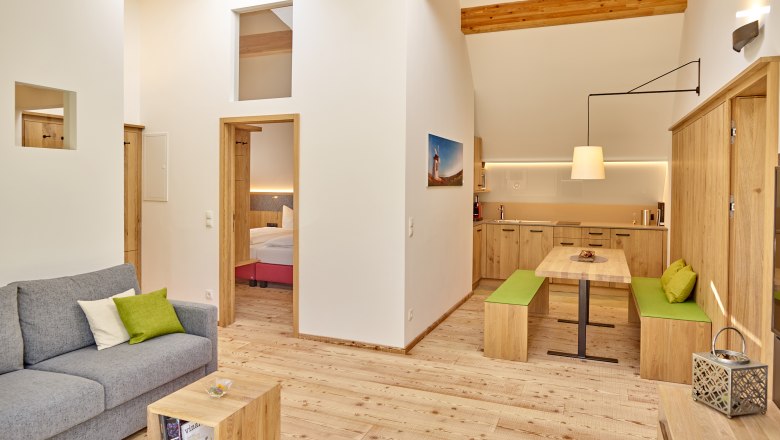 Modernes Wohnzimmer mit Holzm&ouml;beln, grauem Sofa und offener K&uuml;che.