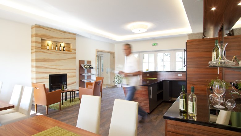 Ein moderner Verkostungsraum mit Holzmöbeln, Weinflaschen und einem unscharfen Mann im Vordergrund.