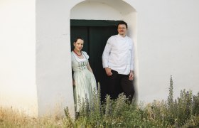 Zwei Personen stehen in einem Türrahmen vor einem weißen Gebäude.