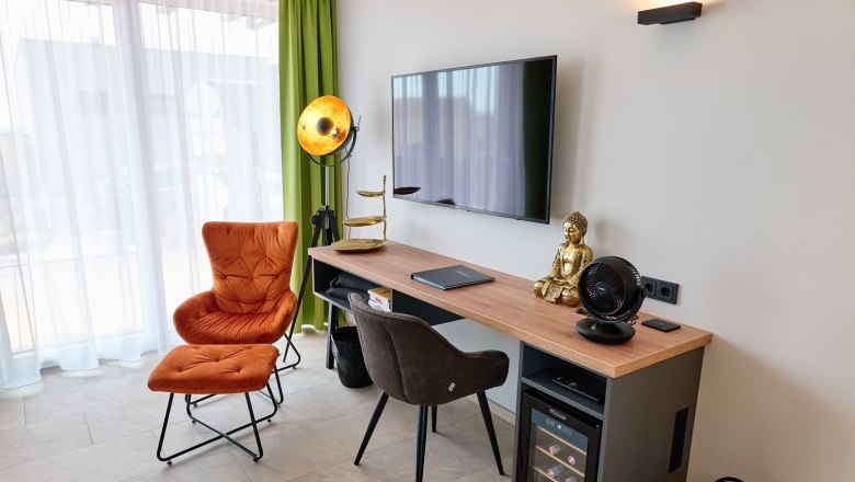 Wohnzimmer mit Sessel, Schreibtisch, Buddha-Statue und Fernseher.