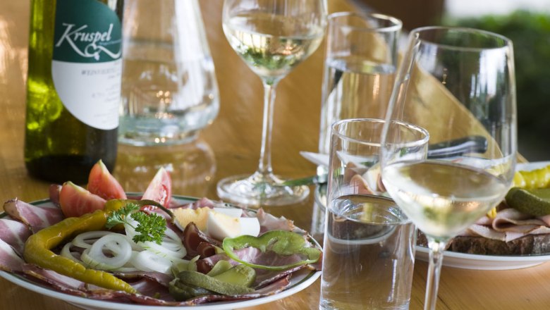Ein gedeckter Tisch mit Heurigenjause, Wein und Wasser.