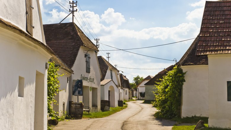 Eine malerische Kellergasse mit weißen Gebäuden und Ziegeldächern unter blauem Himmel.