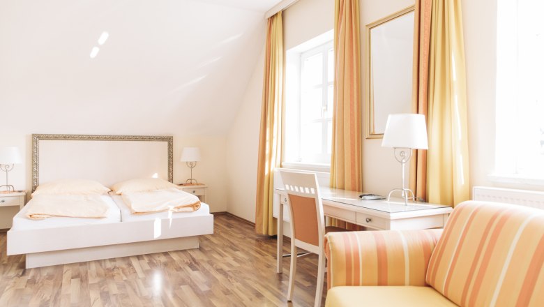 Doppelzimmer, © Agnes Buchmayer Helles Gästezimmer mit Doppelbett, Schreibtisch und Sofa in warmen Gelbtönen.