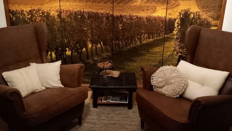 Zwei braune Sessel mit Kissen vor einer Wand mit Landschaftsfototapete eines Weinbergs.