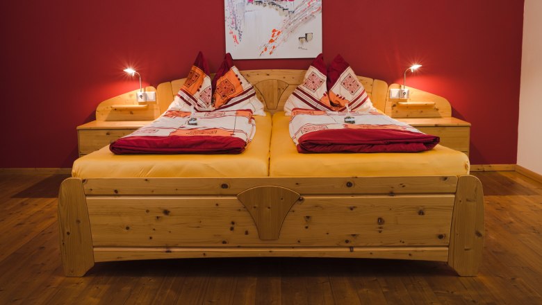 Gemütliches Doppelbett mit roter Wand und Holzfußboden.